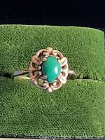 Close-up of the green cabochon stone ring set on green fabric background showcasing detailing of setting and stone color.