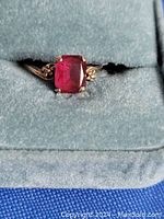 Close-up view of ring in teal velvet box showcasing square-cut deep red garnet center