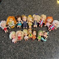 Top-down view of 16 small Liddle Kiddles dolls arranged on countertop, showing variety of hair colors and outfits.