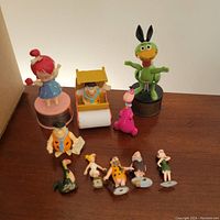 Full view of 1961 Marx Flintstones toy figures including Pebbles push-up puppet, Fred with push roller, green Hoppy figure, pink dinosaur, and multiple smaller character figurines.