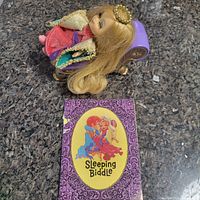 Sleeping Beauty doll lying on its side with storybook next to it showing front cover illustration