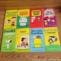 Top view of eight Peanuts softcover books from the 1960s and 70s laid out flat, showing front covers featuring Snoopy, Charlie Brown, and other characters with colorful backgrounds.