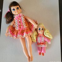 Top view of Angie doll with brown hair and orange dress alongside the smaller Tangie fabric doll in pink outfit and yellow yarn hair.