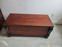 Front view of closed antique cedar chest showing dark wood finish, curved legs, and keyhole.