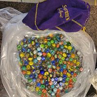 Photo showing the purple Crown Royal bag next to a large clear plastic bag filled with colorful mixed glass marbles.