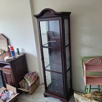 Tall mahogany stained curio cabinet shown from a side angle highlighting glass shelves and overall design.