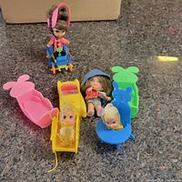 Overview photo of lot showing four dolls and colorful bunny-themed doll furniture pieces including a convertible toy car, reclining chair, and bunny-shaped seats.