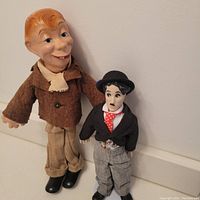 Photo showing Mortimer Snerd and Charlie Chaplin dolls standing side by side against a wall.