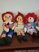 Three Raggedy Ann and Andy dolls seated on wooden surface, showing overall condition and details of each doll.