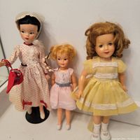 Front view of three vintage dolls including Mary Poppins doll in red polka dot dress, smaller blonde doll in pink dress, and taller curly brown hair doll in yellow dress.