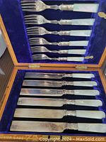 Vintage cutlery set with mother of pearl handles displayed in a blue velvet-lined wooden case. Includes 6 forks and 6 knives.