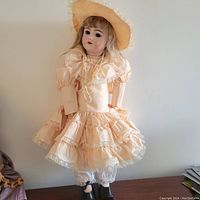 Full view of vintage porcelain doll standing upright, showing dress, hat, and shoes.
