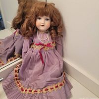Front view of the doll seated against mirror showing full dress detail and auburn curly wig.