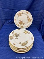 Stack of 8 white bone china plates with gold floral patterns and scalloped edges with gold rims