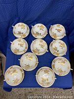 Top view of 10 soup cups and saucers laid out on blue fabric background.