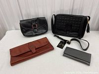 Four leather items: two handbags and two wallets on a white surface