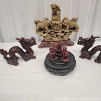 Front view of all five sculptures: central lion sculpture on wooden base, two dragon sculptures on each side, and small figurine group in front on round wooden base.