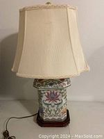 Full view of vintage chinoserie style table lamp showing cream fabric shade, ceramic base with painted floral decor and wood base platform.