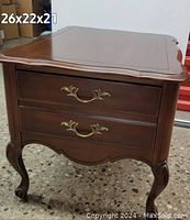Front view of mahogany French Provincial end table showing two drawers with brass handles and carved cabriole legs.