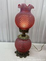 Front view of the lamp showing the cranberry hobnail glass globes on top and bottom and metal base.