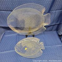 Two glass fish platters displayed against blue fabric; one large and one medium; detailed scale and fin textures visible.