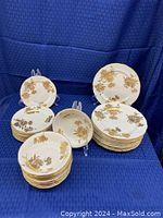 Full view of plates and bowls grouped in stacks, showing gold floral designs on white fine china with scalloped edges and gold trim.