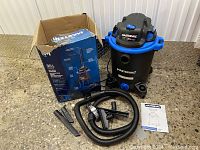 Full view of the Mastervac shop vacuum with hose, attachments, instruction manual, and packaging box on floor.