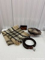 Photo showing all four items: wool scarf/throw folded, brown bi-fold wallet, braided brown leather belt, and checkered flat cap.