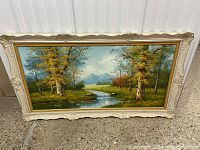 Front view of the framed large oil landscape painting with river, trees, mountains, and cloudy sky.