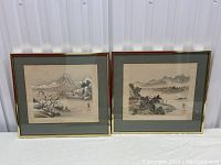 Frontal image showing both framed silk paintings with gold frames and greenish mats.