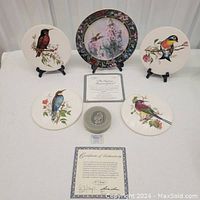 Full view of all six porcelain bird trivets displayed with the Swarovski bird figurine and the signed collector plate.