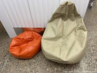 Side view of the two vintage bean bag chairs against a warehouse wall with concrete floor, showing the size difference and material texture.