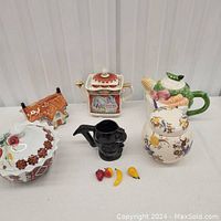 Overview of assorted vintage ceramic teapots, bowl, cup, and fruit ornaments on a white surface.