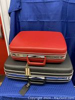 Two stacked vintage Samsonite hard-shell suitcases, one red on top and black below, against a blue fabric background.