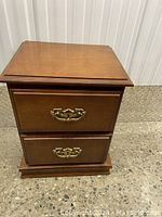 Front view of the solid wood nightstand showing two closed drawers with brass handles in very good condition.