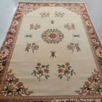 Full photo of cream background rectangular wool area rug. Floral central medallion with surrounding floral clusters and abstract symbols. Wide border with floral pattern in warm colors and Greek key design.