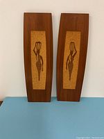 Pair of wood and cork wall art panels side by side on blue surface, showing both figures in full.