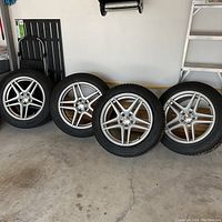 Four silver RTX alloy rims with Continental WinterContact SI tires leaning against garage wall