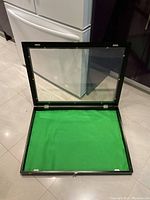 Open display case showing green felt interior and wooden frame with plexiglass top.