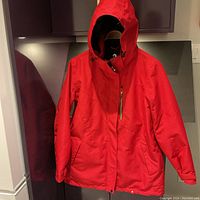 Front view of red Ripzone winter jacket hanging on a door, showing zippered pocket and hood