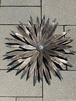 Metal sunburst shaped wall decor with layered pointed copper petals and a round center, laid on stone tiles showing its size and texture.