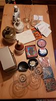 Overview of ceramic and glass decanters, assorted glasses, boxed lobster pick set, colorful coasters, ashtrays, and copper enamel dishes on table.