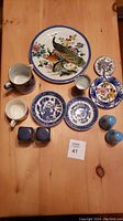 Top view of all pottery items arranged on wooden table, showing peacock plate, French pitcher, willow pattern plates, small floral dishes and salt and pepper shakers.