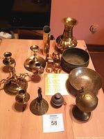 Photo of assorted brass items on wooden table including candleholders, bowls, napkin rings, bells, a globe and vases.