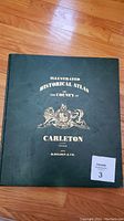 Front cover of the Illustrated Historical Atlas of the County of Carleton showing dark green cover with gold embossed text and coat of arms