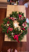 Full top view showing the Christmas wreath on a wooden surface with visible red velvet ribbon and glittery ornaments.