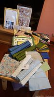 Photo showing assorted folded and rolled dining linens including solid greens, blue stripes, and fringed linens near packaged napkins.