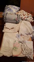 Crocheted round tablecloth, embroidered cloths, bolster pillow, and a modern toile cushion.