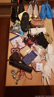Wide view of assorted ladies' accessories laid out on table including footwear (black patent leather shoes, black ballet flats, cream high heels, bright blue woven shoes), gloves in beige, black and white, various jewelry pieces, multiple trinket boxes, scarves, sunglasses, and DVD.