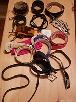 Photo showing an array of eleven ladies' belts of different styles and colors laid on wooden surface, including a patent belt with brass buckle, black leather belts, and fabric belts.